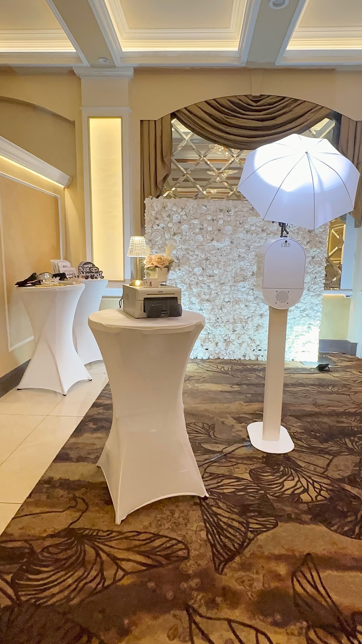 The Sweet Moments photo booth set up in a ballroom with a white flower wall, printer and props table